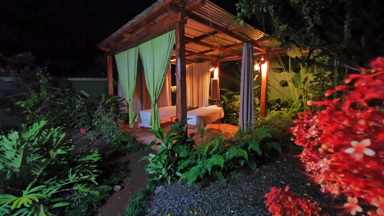 El pabellón de masajes de noche, iluminado entre plantas tropicales y flores rojas